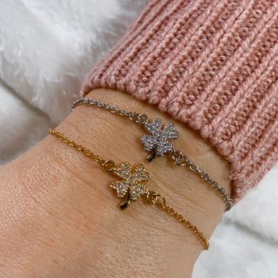 Dois braceletes, dourado e prateado, com pendentes de trevo brilhantes num pulso com camisola rosa
