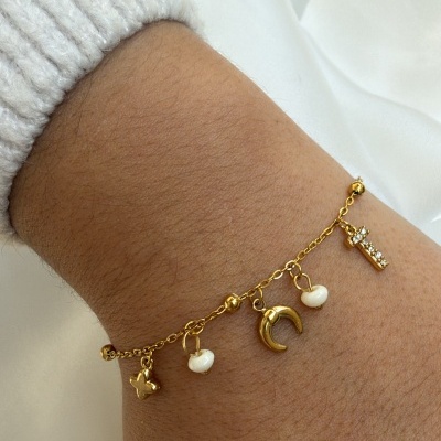 Pulseira dourada com pendentes variados no pulso
