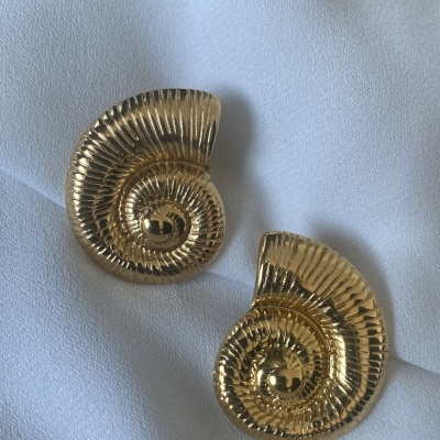 Brincos dourados em forma de concha com textura estriada sobre tecido branco