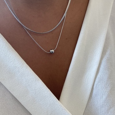 Colar duplo prateado com pendente esférico sobre roupa branca