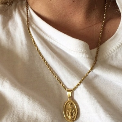 Colar dourado com pingente religioso usado numa t-shirt branca