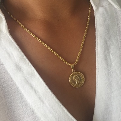 Colar dourado com pendente redondo em relevo usado com camisa branca