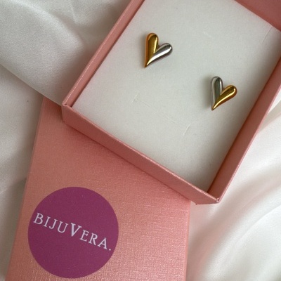Brincos em forma de coração dourado e prateado numa caixa rosa sobre tecido branco