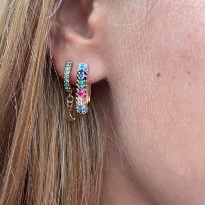 Brincos de argola dourados com pedras coloridas em orelha de pessoa loira