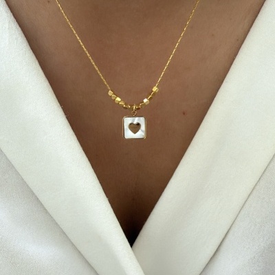 Colar dourado com pingente quadrado e coração recortado numa blusa branca