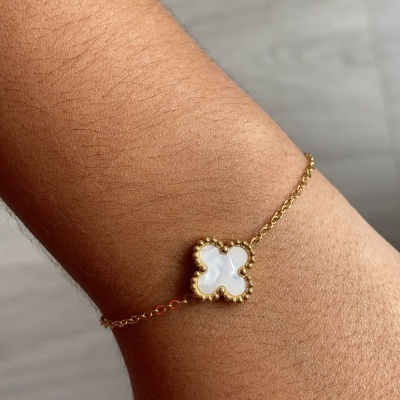 Pulseira dourada com pendente de flor madre-pérola no pulso.