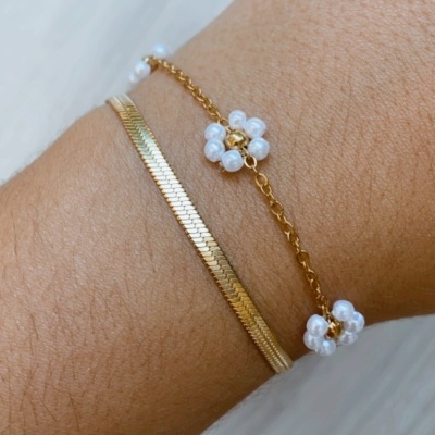 Pulseira dupla dourada com flores de pérolas brancas num pulso