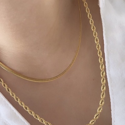 Dois colares dourados, um fino liso e um grosso entrelaçado, em pescoço com roupa branca