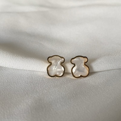 Brincos em forma de ursinho em madrepérola com contorno dourado sobre tecido branco.