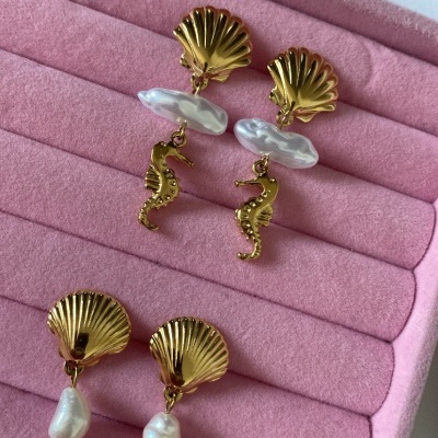 Dois pares de brincos dourados com conchas e pérolas sobre estojo rosa