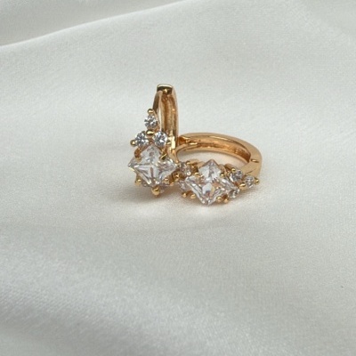 Brincos dourados com pedras quadradas e cristais sobre tecido branco acetinado