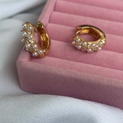 Brincos dourados com pérolas numa caixa rosa sobre tecido branco