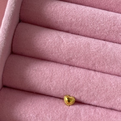 Anel dourado em forma de coração numa caixa de veludo rosa com rolos para anéis