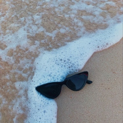 Óculos de sol pretos em forma de gatinho na areia molhada com espuma do mar