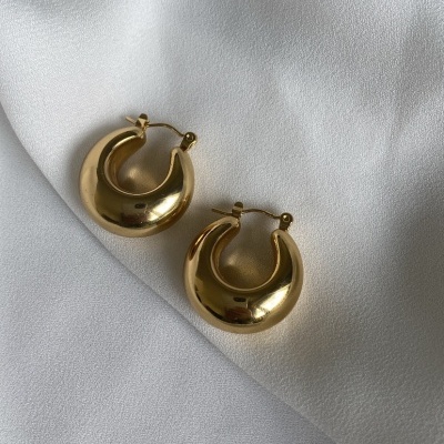 Brincos dourados tipo argola sobre tecido branco