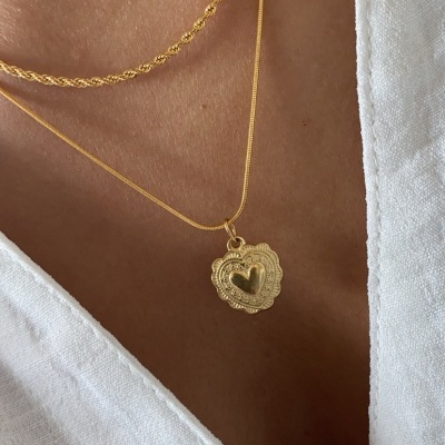 Colar dourado com pingente de coração usado sobre pele e roupa branca