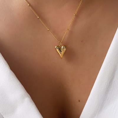 Colar dourado com pendente em forma de coração em pescoço com camisa branca