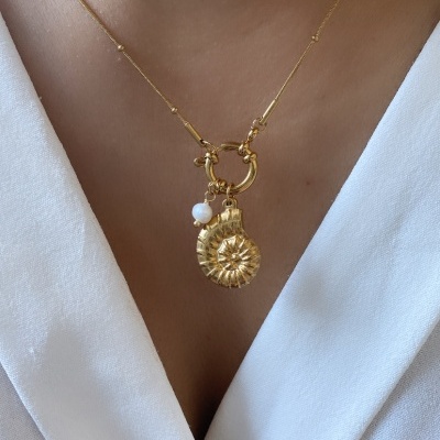 Colar dourado com pendente concha e pérola sobre blusa branca
