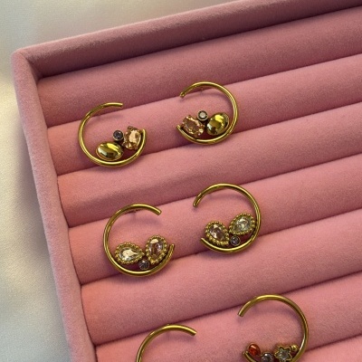 Três pares de brincos dourados com pedras numa caixa de veludo rosa