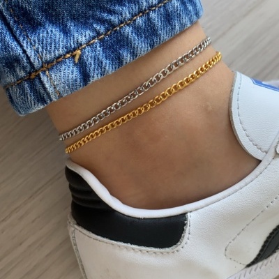 Tornozelo com pulseiras prateada e dourada, jeans azul e ténis brancos com detalhes pretos.