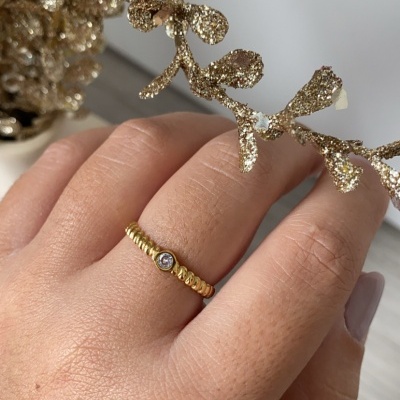 Anel dourado com pedra pequena numa mão perto de decoração dourada.