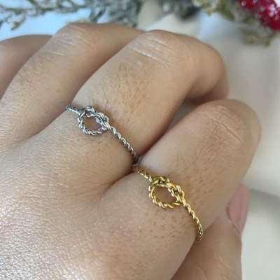 Dois anéis torcidos, um prata e outro dourado, com nó no centro em dedos da mão