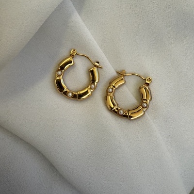 Brincos argola dourados com pérolas sobre tecido branco