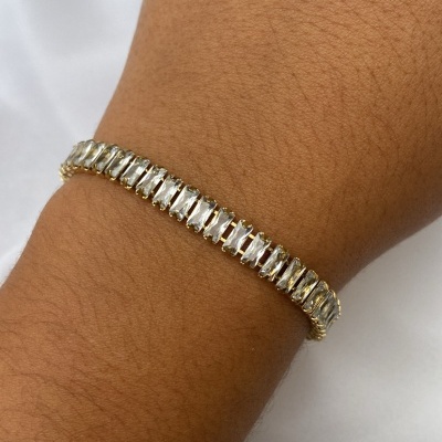 Pulseira dourada com pedras retangulares transparentes no pulso
