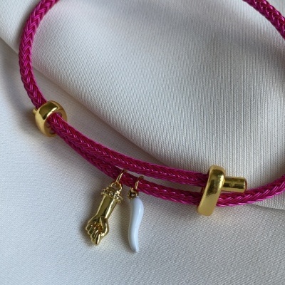 Pulseira de corda rosa com pendentes dourado e branco sobre tecido branco
