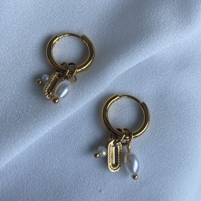 Brincos de argola dourados com pendentes de pérola e placa retangular sobre tecido branco