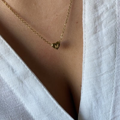Colar dourado com pendente em forma de coração com letra M e camisa branca