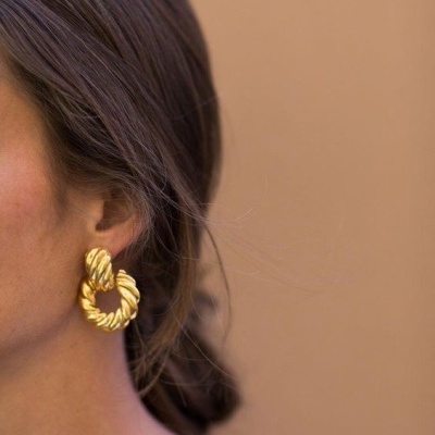 Brincos torcidos dourados em orelha de mulher com cabelo castanho