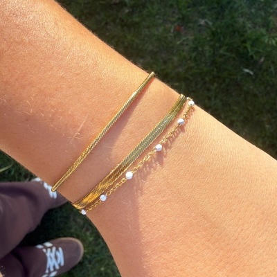 Pulseira dourada com três correntes finas e pequenas pérolas brancas ao pulso