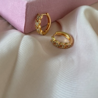 Brincos dourados com pedras em tecido branco com caixa rosa