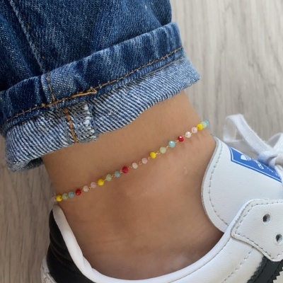 Tornozeleira colorida com contas pequenas no tornozelo com calças de ganga e sapatilhas brancas