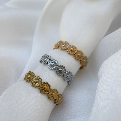 Três anéis florais metálicos em dourado e prateado sobre tecido branco.