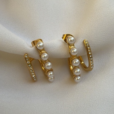 Brincos dourados com pérolas e pedras brilhantes sobre tecido branco