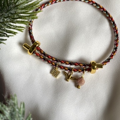 Pulseira trançada colorida com pingentes dourados e pedra rosa sobre tecido branco