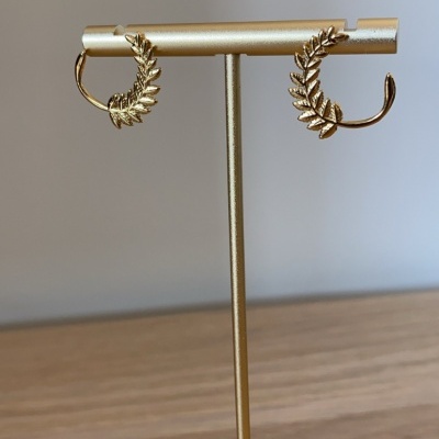 Brincos dourados com design de folhas num suporte dourado