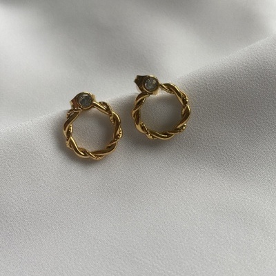 Par de brincos dourados com pedra transparente sobre tecido branco