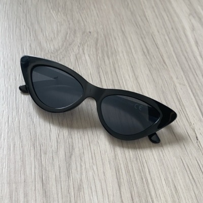 Óculos de sol pretos estilo gatinho sobre superfície de madeira clara