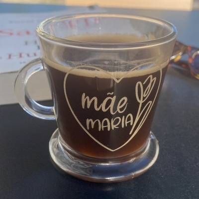 Cálice de vidro com café e texto 'mãe MARIA' impresso em branco
