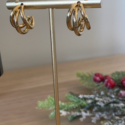 Brincos de argola dourados expostos num suporte dourado sobre mesa