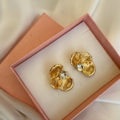 Brincos dourados com pedra brilhante em caixa cor de rosa sobre tecido branco