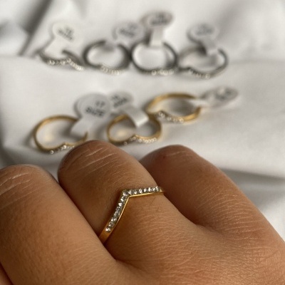 Anel dourado com pedras brilhantes em formato V na mão, outros anéis semelhantes ao fundo