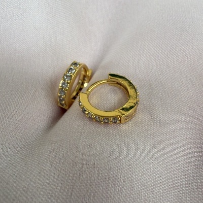 Brincos de argola dourados com pedras brilhantes sobre tecido creme