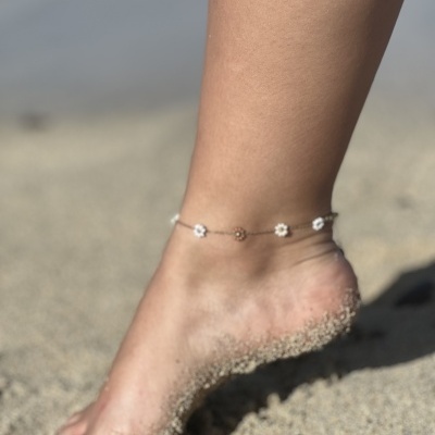 Tornozeleira com flores pequenas num pé na praia, parcialmente coberto de areia