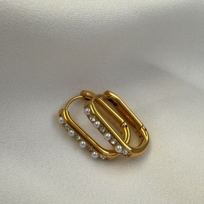 Brincos dourados retangulares com pérolas sobre tecido branco