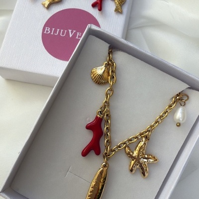 Conjunto de joias douradas com pingentes marinhos e pérolas em caixas brancas