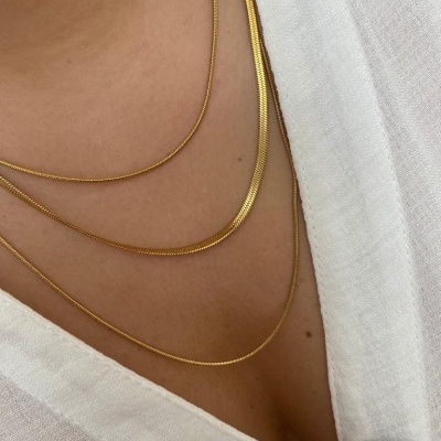 Colares dourados finos usados sobre blusa branca com botão marrom